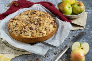 Einfacher gedeckter Apfelkuchen mit Nüssen. Kuchen auf dem Rost. Äpfel in einer Schale.